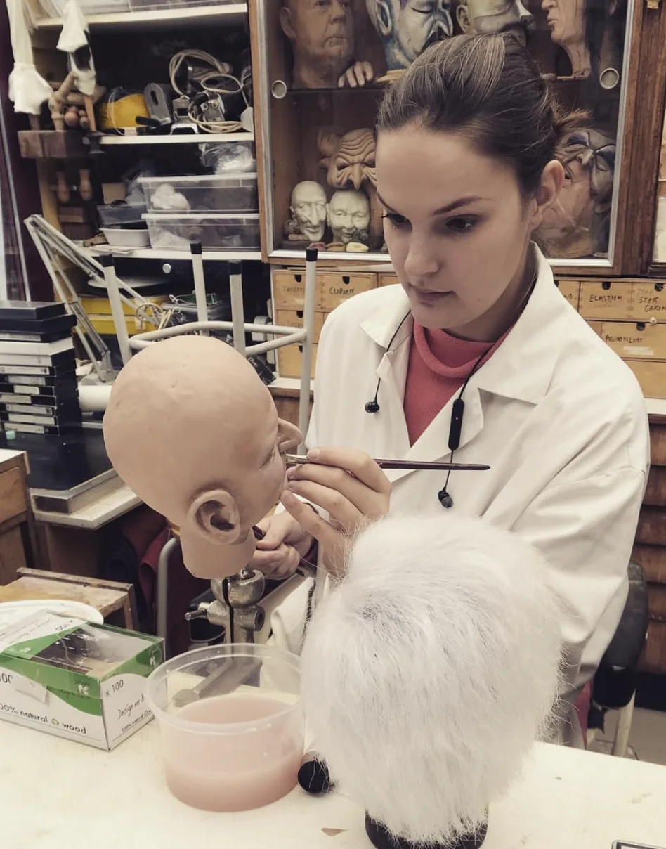 Een vrouw werkt met een penseel aan een hoofdmodel in een atelier.